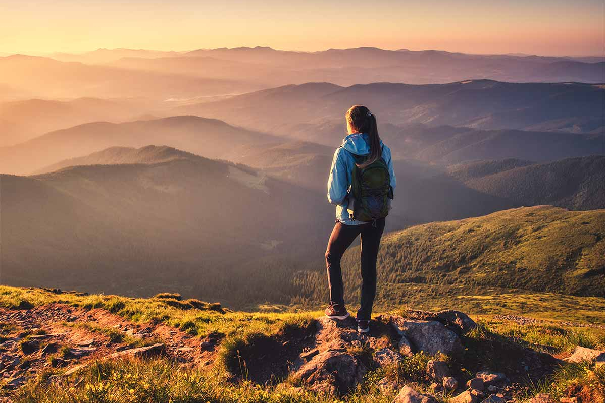 Wanderin steht auf dem Berggipfel und blickt auf die umliegenden Bergketten