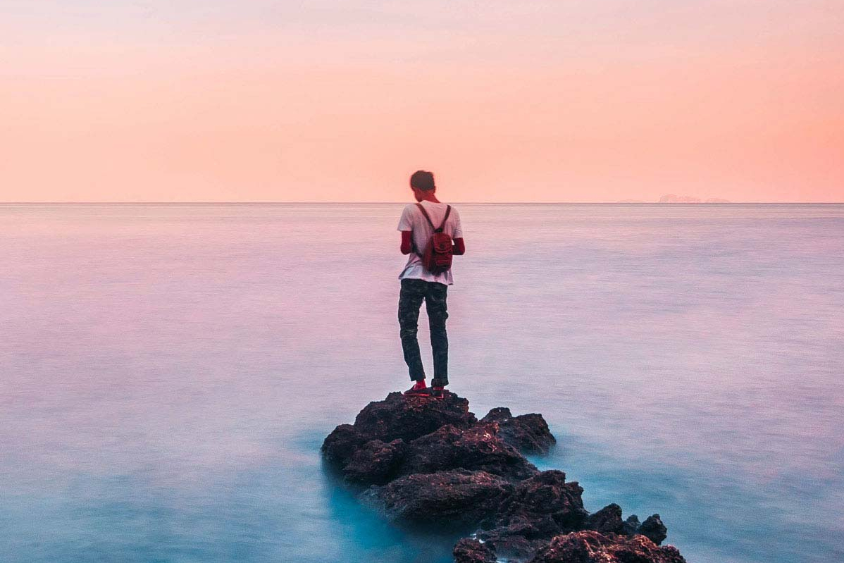 Mann steht auf einem Felsen im Meer und blickt in die Ferne