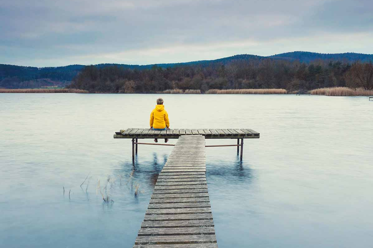 Person sitzt auf einem Steg und blickt auf den See