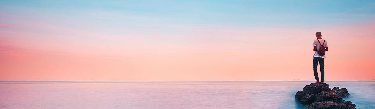 Mann steht auf einem Felsen im Meer und blickt in die Ferne